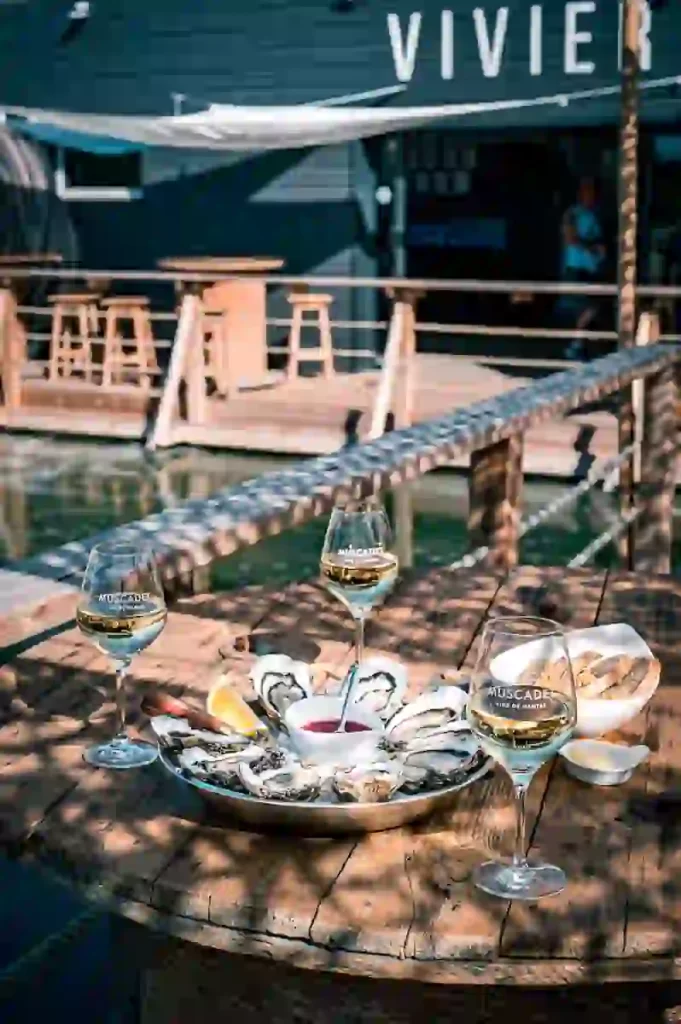 生牡蠣の盛り合わせとミュスカデワインが入ったグラスが3杯、海沿いの外の風景