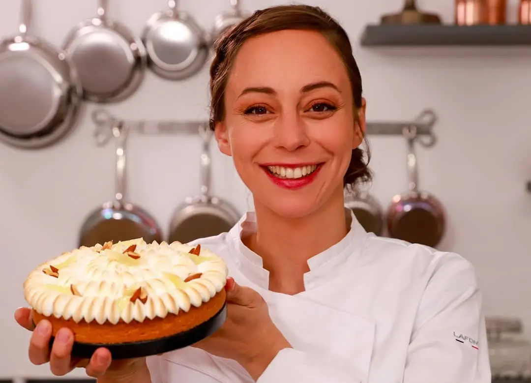 nina metayer ニーナ・メタイエが笑顔で、ケーキ菓子を持って厨房に立っている
